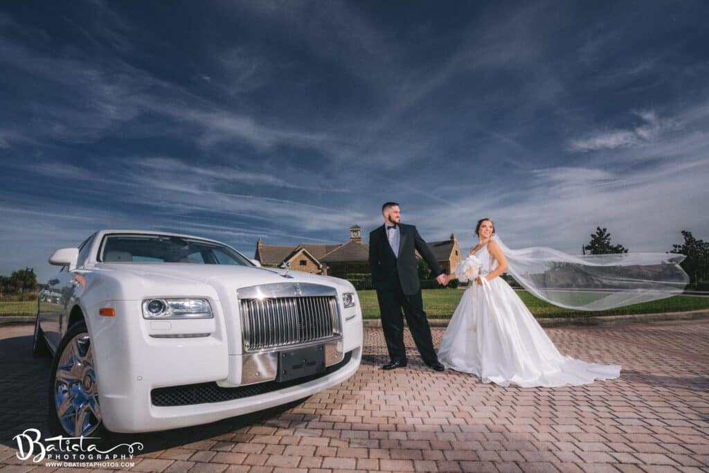 Bride and groom stand next to the Rolls Royce Ghost courtesy of Exotic Limo Orlando.