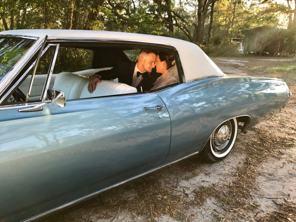 Bride and groom sitting in the classic 68 Chevy Impala.