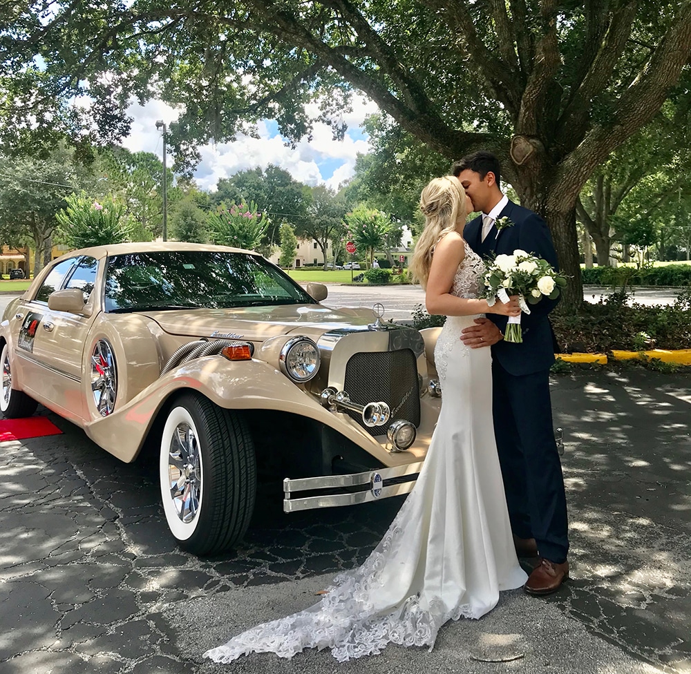 Bride and groom kiss in front of their wedding limo, the Excalibur Godfather.