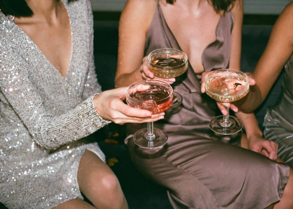 Three women clink champagne glasses together in a limo during a bachelorette party