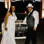 Bride and groom standing with the Rolls Royce Ghost under Champions Gate sign