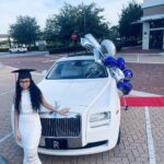 A young girl in graduation cap poses with the Rolls Royce Ghost