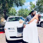 Bride and groom kiss with bride's bouquet resting on the Rolls Royce Ghost