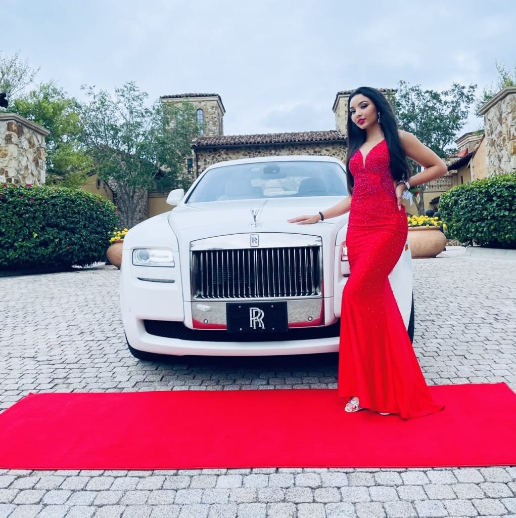 A young girl standing on red carpet next to the Rolls Royce Ghost limousine