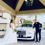 Bride and groom pose outside their wedding venue with their wedding car, the Rolls Royce Ghost.