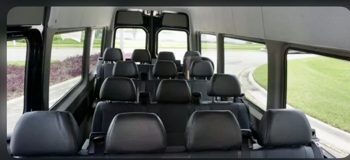 The interior view of our Mercedes passenger van, showcasing the 14 passenger capacity. The seats are black leather. There are 4 rows with the front most row having 4 seats, the 2 middle rows having 3 seats each, and the final row having 4 seats. 