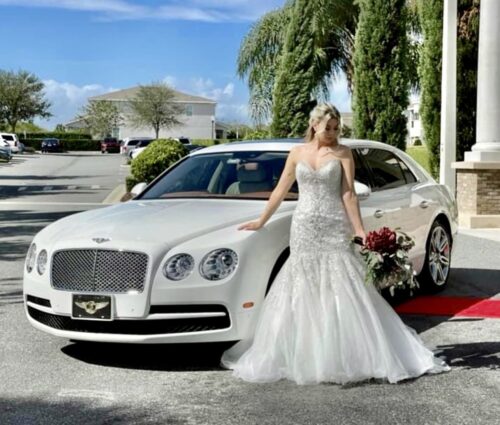 A bride posing in front of a white Bentley.