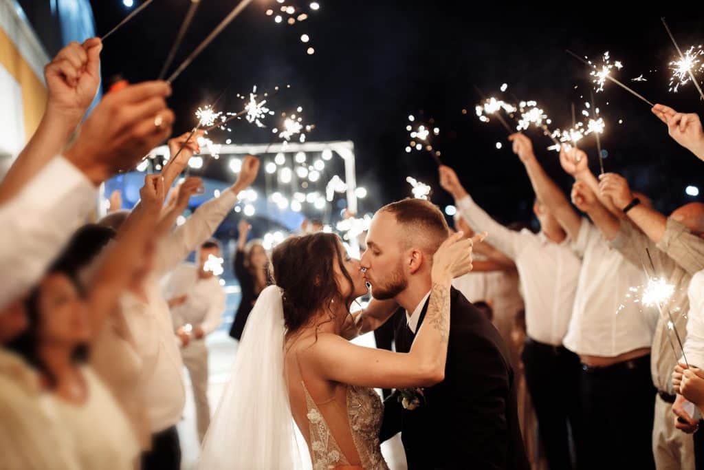 Bride and groom kissing as guests hold sparklers over them for their wedding send off