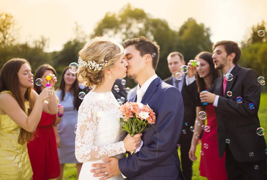Bride and Groom kissing while guests blow bubbles for their wedding send off